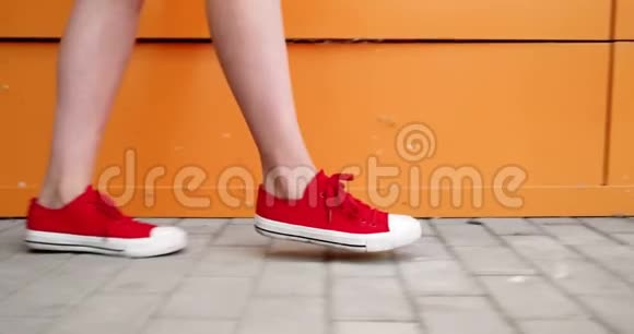 女足穿着运动鞋胶鞋沿着橙色的墙走近距离女穿着红色运动鞋走路的脚视频的预览图