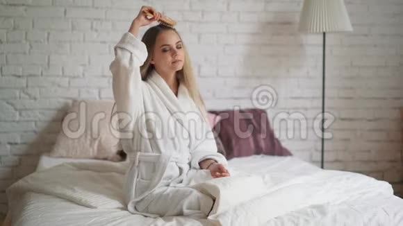 快乐的女人穿着浴衣在卧室梳着美丽的长发视频的预览图