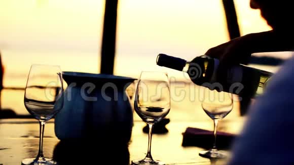 在令人惊叹的日落时分在海滩餐厅的海景中在玻璃杯中倒入白酒1920x1080视频的预览图