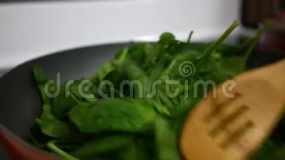在加热的锅里用木勺搅拌枯萎的菠菜视频的预览图