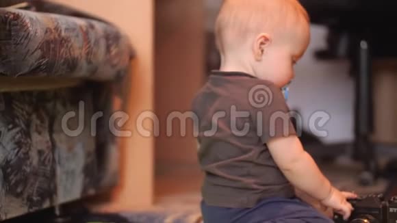 一个嘴里含着肥皂的婴儿坐在地板上摸着一台旧相机然后转过身来4K室内侧景视频的预览图