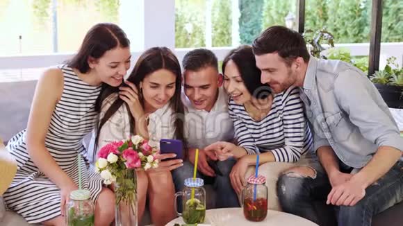 一群朋友在看着坐在咖啡馆里的手机照片时笑了视频的预览图