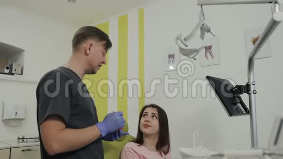 美丽的年轻病人坐在牙医的椅子上微笑一位英俊的牙医用人工下巴视频的预览图
