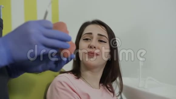 美丽的年轻病人坐在牙医的椅子上微笑一位英俊的牙医用人工下巴视频的预览图