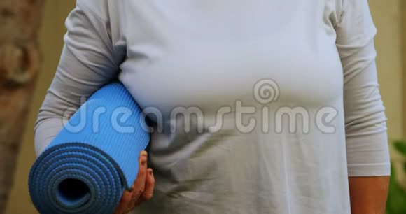 4K花园里一位手持瑜伽垫的年长妇女微笑视频的预览图