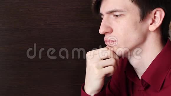 一个穿红色衬衫的年轻人把下巴靠在右臂上视频的预览图