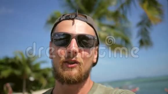 在海滩上的智能手机上年轻的大胡子牛仔视频聊天在手机上聊天和做自拍高清慢镜头视频的预览图