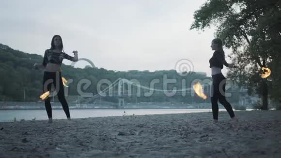 两个年轻女子站在河岸上表演火焰球有技巧的女艺术家表演视频的预览图