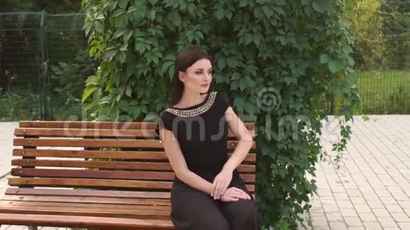 穿着黑衣服的女孩坐在公园的长凳上视频的预览图