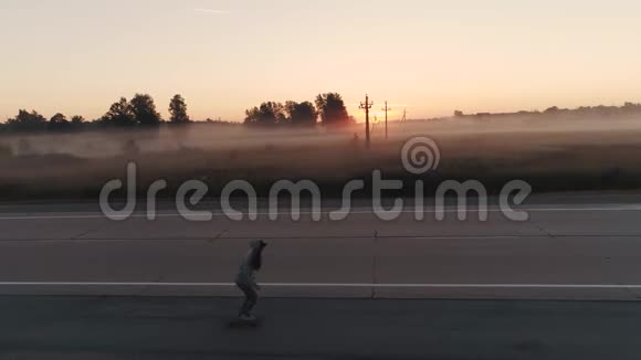 空中飞行一个十几岁的女孩在黎明时沿着城外的一条荒无人烟的上滑冰穿着运动衫的年轻女孩视频的预览图