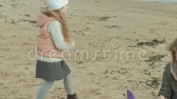 年轻的女人穿着外套有一个卷发的女孩妈妈和女儿坐在河边的海滩上海洋里有一个女孩视频的预览图