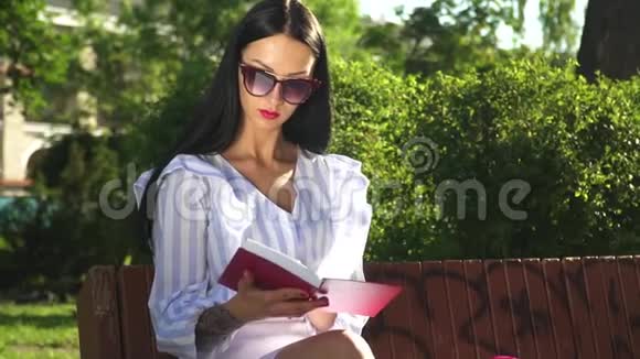 戴太阳镜的时髦女人在公园看书视频的预览图
