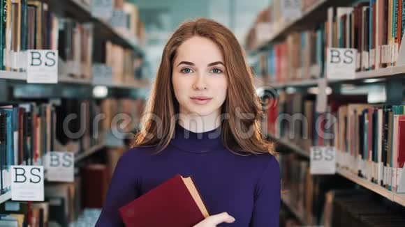 留着长发的女孩微笑着直视着图书馆书架前的镜头视频的预览图
