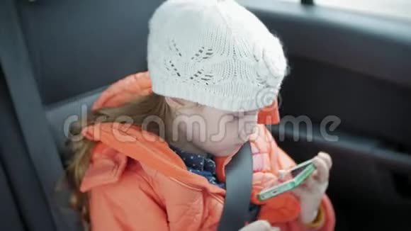 小女孩微笑着用智能手机分享社交媒体她在车里旅行视频的预览图