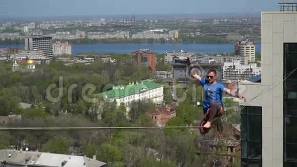 一个穿着蓝色T恤的男人在一个巨大的高度上挂在一根紧绳上视频的预览图