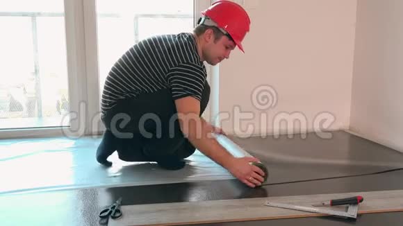 安装强化木地板用带红色头盔铺设垫层的施工员视频的预览图