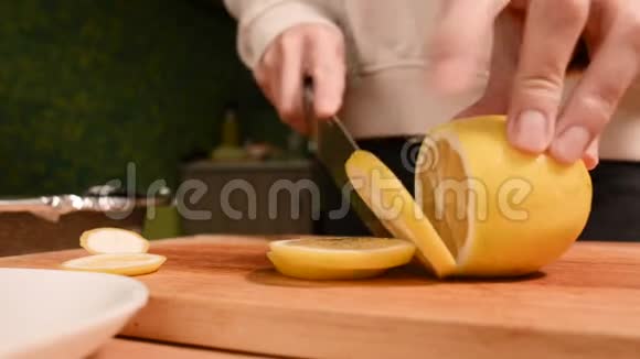 在家厨房的一个女孩的手在一个木切割板上特写在婴儿车上切一个黄柠檬家庭视频的预览图