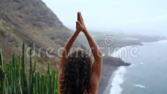 年轻女子在山上做瑜伽在一个岛屿上俯瞰大海坐在山顶的岩石上视频的预览图