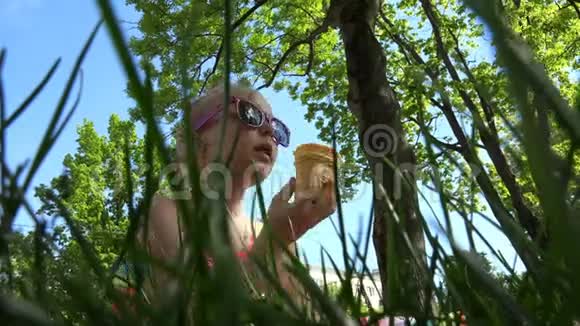 一个戴太阳镜的女孩正在公园树下吃一把伞视频的预览图