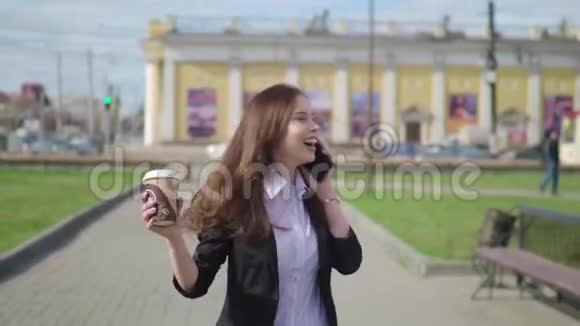 美丽的黑发女人走在城市的街道上用手机说话带着咖啡走的女人视频的预览图