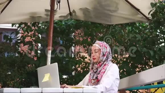 穆斯林妇女戴着头巾在笔记本电脑上打印信息她在外面露天视频的预览图
