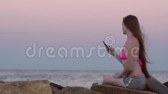 沙滩上穿泳衣的女孩坐在岩石上不停地拨电话号码视频的预览图