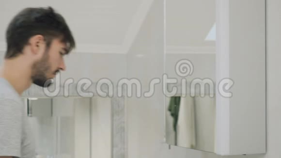 年轻的困倦者在镜子前用牙刷清洁牙齿视频的预览图