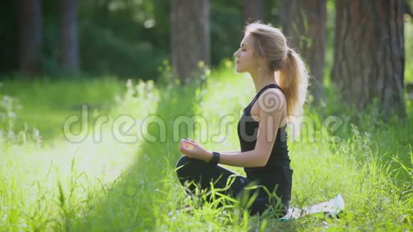 在公园外面做瑜伽的女人她坐在莲花的姿势上视频的预览图