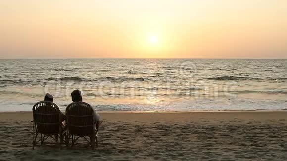 一对欣赏日落的夫妇坐在靠近海岸线的扶手椅上视频的预览图