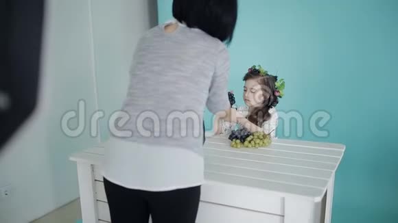 小女孩拿着葡萄摆姿势给坐在桌边的摄影师拍照视频的预览图
