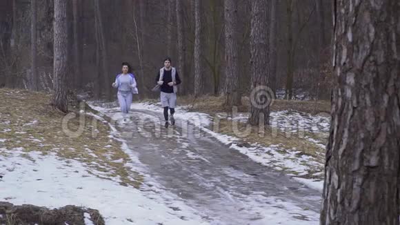 一个年轻的女人和一个男人在森林里滑滑的冬季道路上奔跑视频的预览图