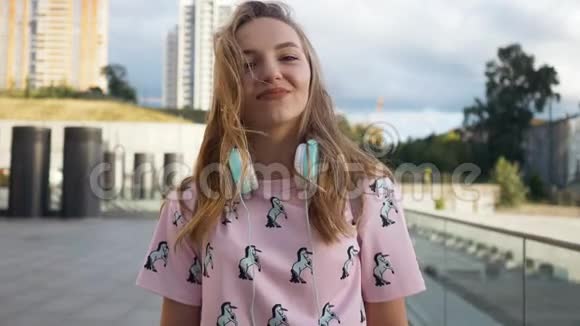 慢镜头肖像迷人可爱微笑的白种人年轻女子带耳机和背包在城市视频的预览图