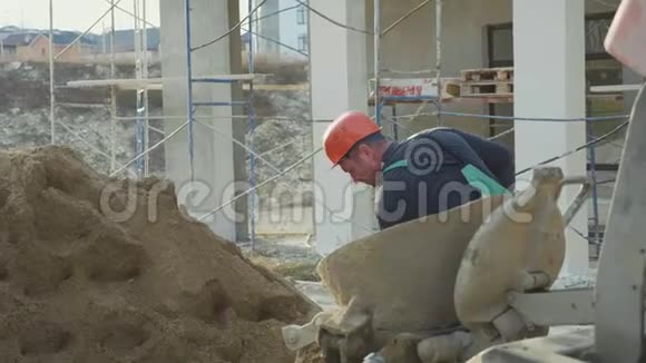 白种人工人在施工现场用铲子将沙子倒入混凝土搅拌机中视频的预览图