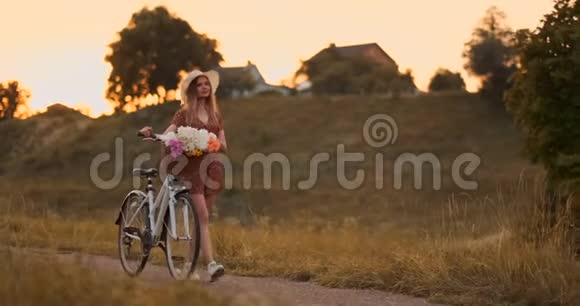 穿着连衣裙的年轻女孩骑着自行车和鲜花在路上行走视频的预览图