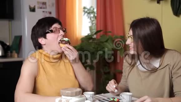 妈妈和带眼镜的小女儿在厨房里喝茶或咖啡吃蛋糕说话笑视频的预览图