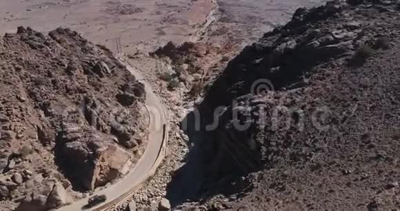 在山路上行驶的黑色汽车的鸟瞰图无人驾驶飞机飞过碎石路视频的预览图