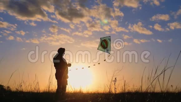 一个幸福的家庭玩风筝的剪影爷爷和小女孩在日落时玩风筝视频的预览图