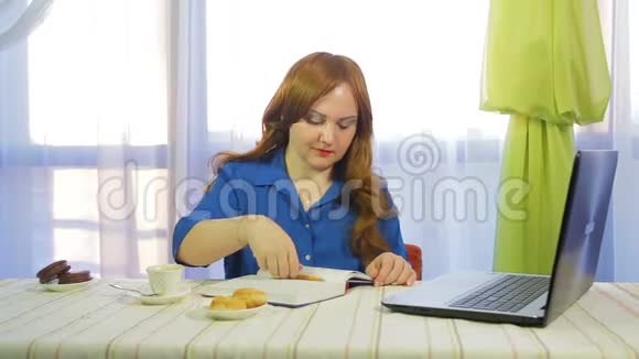 一个棕色头发的女人在一张桌子上的咖啡馆里工作拿着笔记本电脑喝咖啡视频的预览图