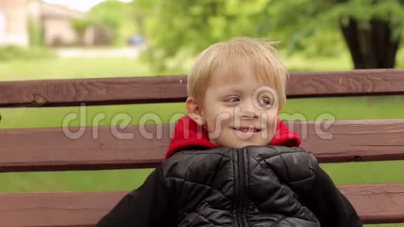 公园里一个微笑的男孩在长凳上的肖像视频的预览图