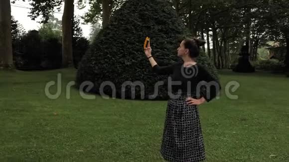 美丽的女孩穿着黑色手工服装用她的移动智能手机在仙女尾林花园绿色视频的预览图
