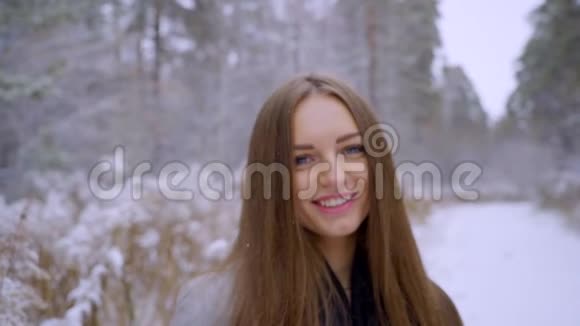 在雪地背景下的冬季公园里一个时尚快乐的年轻漂亮女人的近照期待视频的预览图