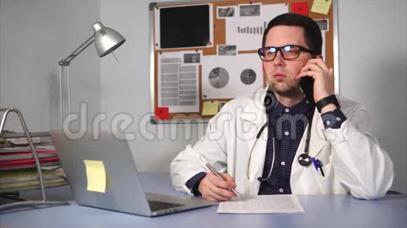 诊所里的男医生坐在办公桌前用智能手机说话视频的预览图