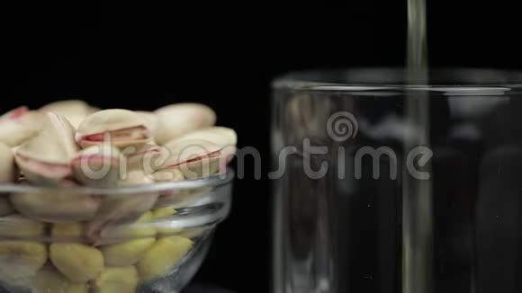 啤酒在黑色背景下倒入玻璃中开心果果碗视频的预览图