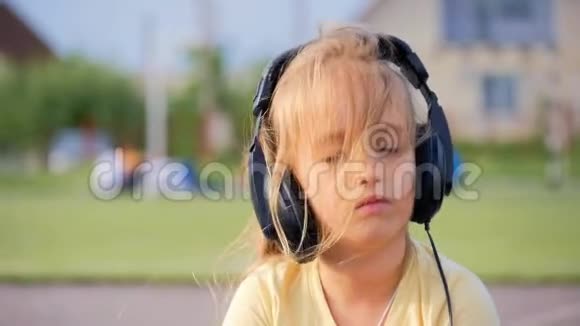 快乐的小女孩在阳光明媚的日子里用耳机听音乐视频的预览图
