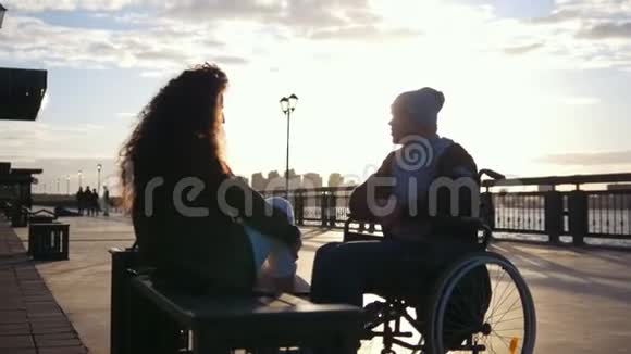 快乐的一对残疾的年轻人坐在轮椅上年轻女子一起享受日落视频的预览图