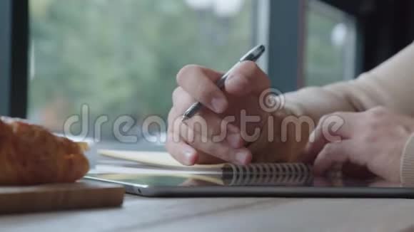 活跃的男人在咖啡馆工作记笔记看平板电脑视频的预览图