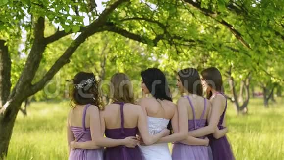 从情感的新娘和伴娘背后看他们说话微笑穿紫色裙子摆姿势的白人女孩视频的预览图