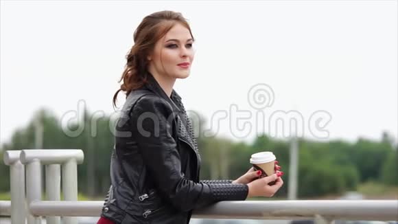 一个穿着皮夹克手里拿着咖啡的浪漫女人把目光移开视频的预览图