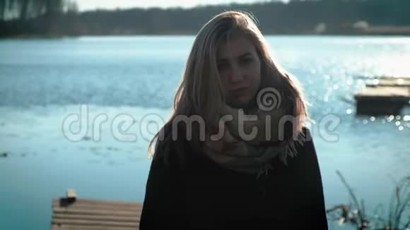 一个身穿外套的金发美女站在湖边的码头上湖面上秋天和多云的心情视频的预览图
