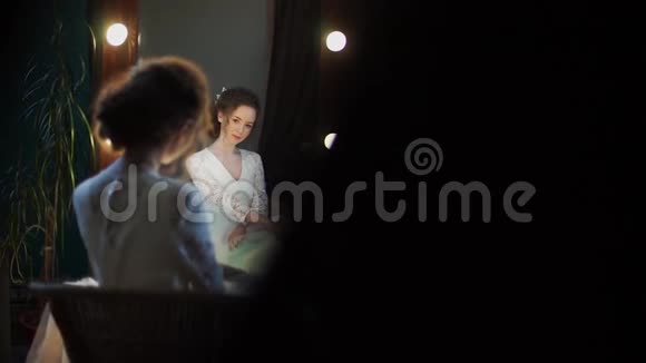 美丽的新娘模特坐在镜子前用手伸直婚纱视频的预览图